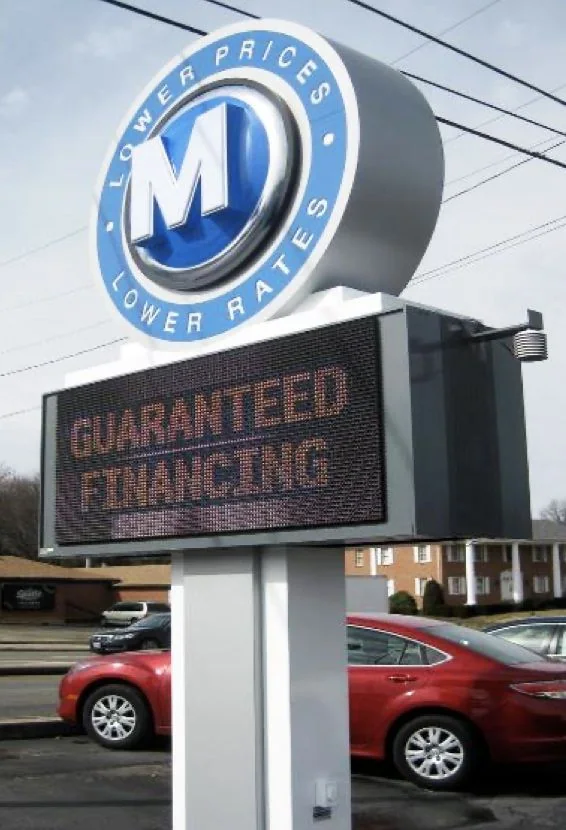 Illuminated cabinet sign with a circular logo on an automotive storefront